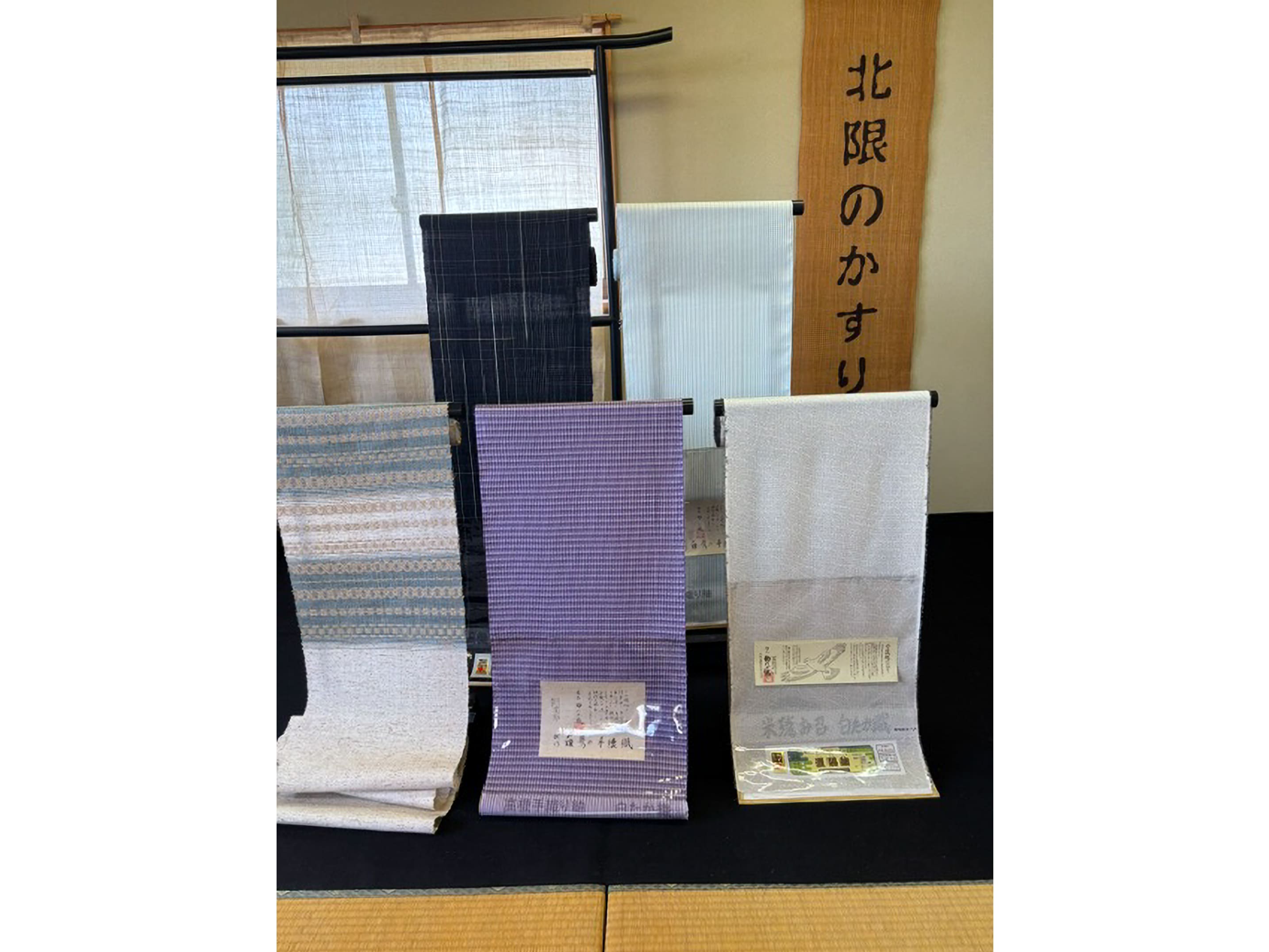 「北限のかすり」の看板とともに展示された、緻密な小絣模様や縞模様が美しい白鷹織の反物 