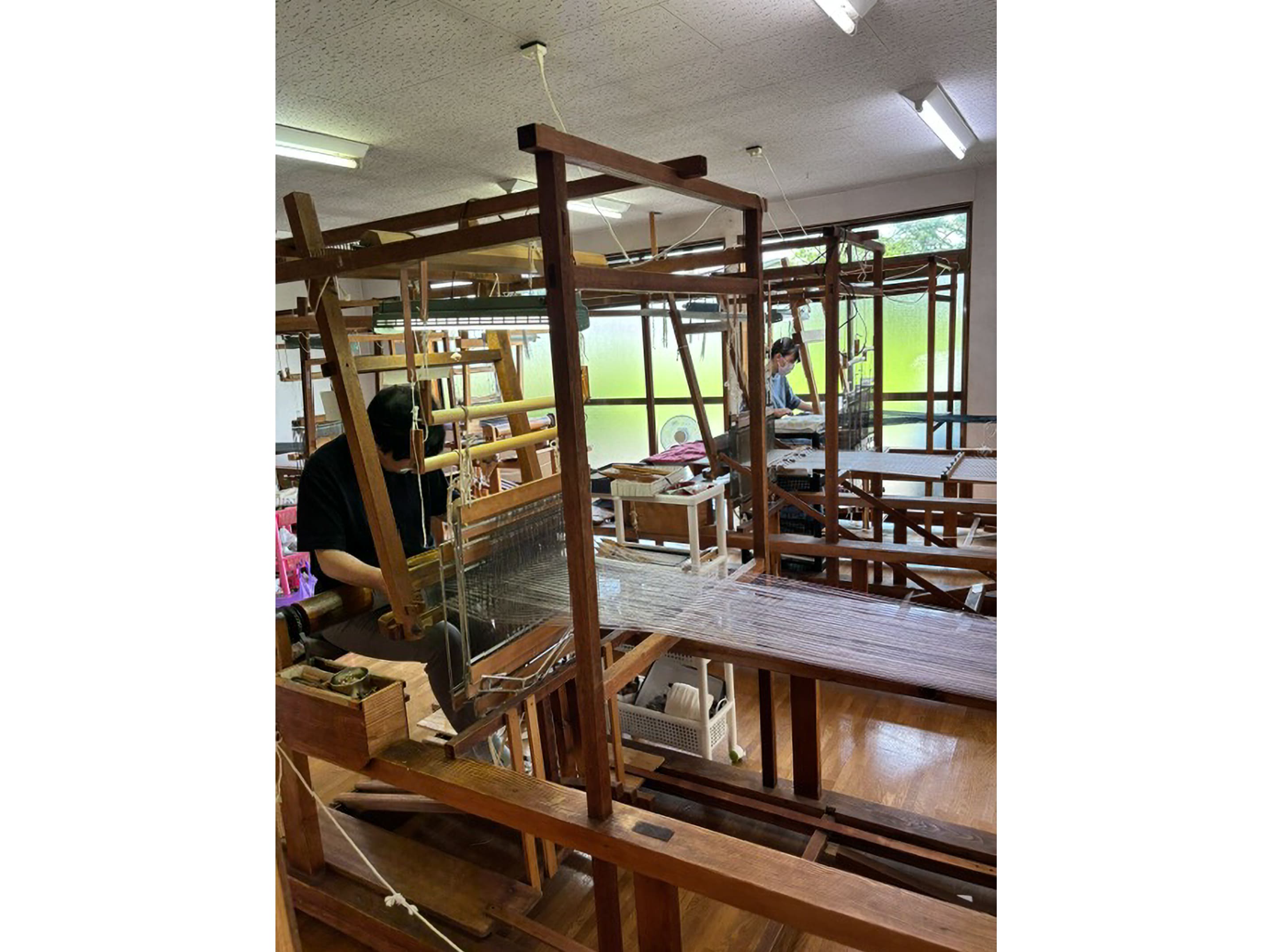昔ながらの大きな木製高機（たかばた）に向かい、一本一本丁寧に糸を打ち込んでいく職人の手織り風景 