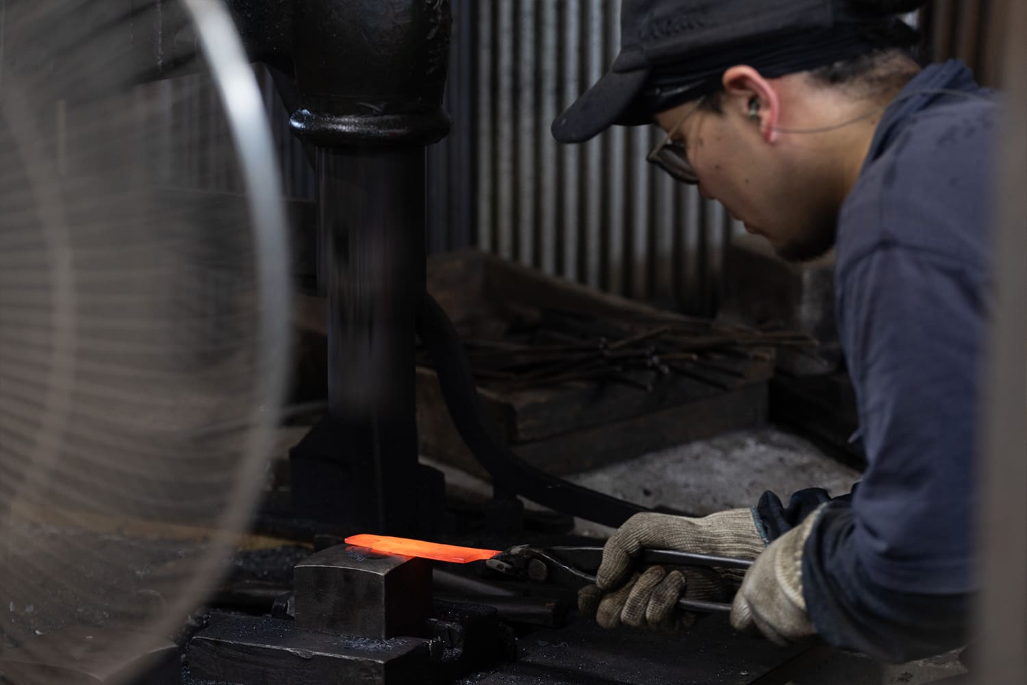 熱した鉄材を機械で打つ鍛冶の作業風景 